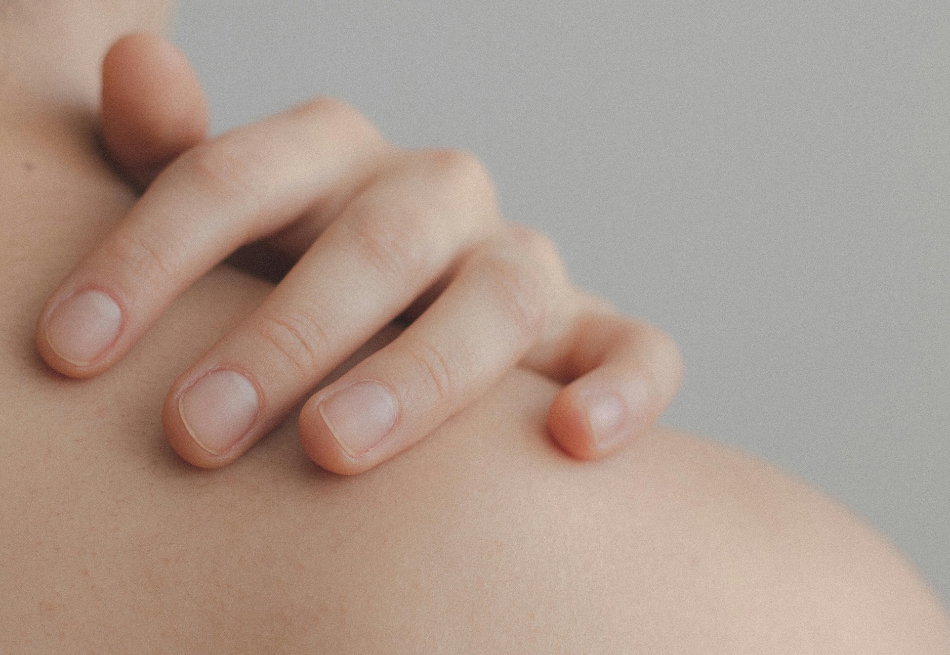 A close-up image of a person's hand gently resting on their shoulder.