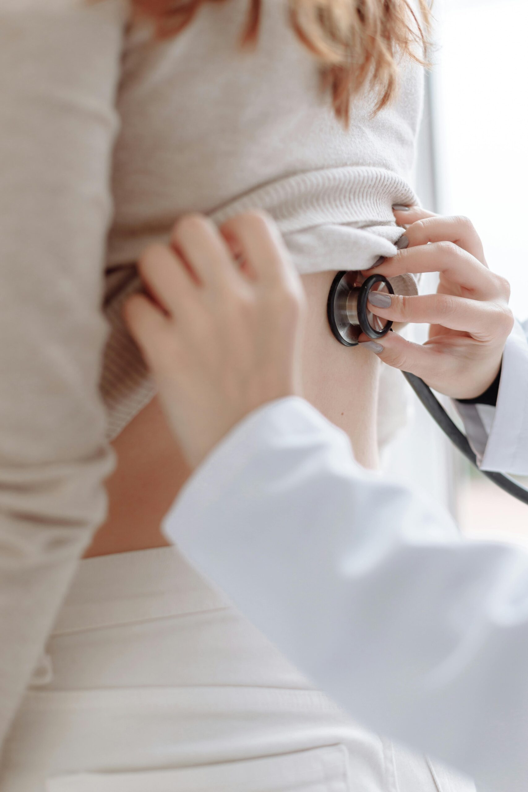 A close up of a doctor placing a stethoscope onto a ladies back.
