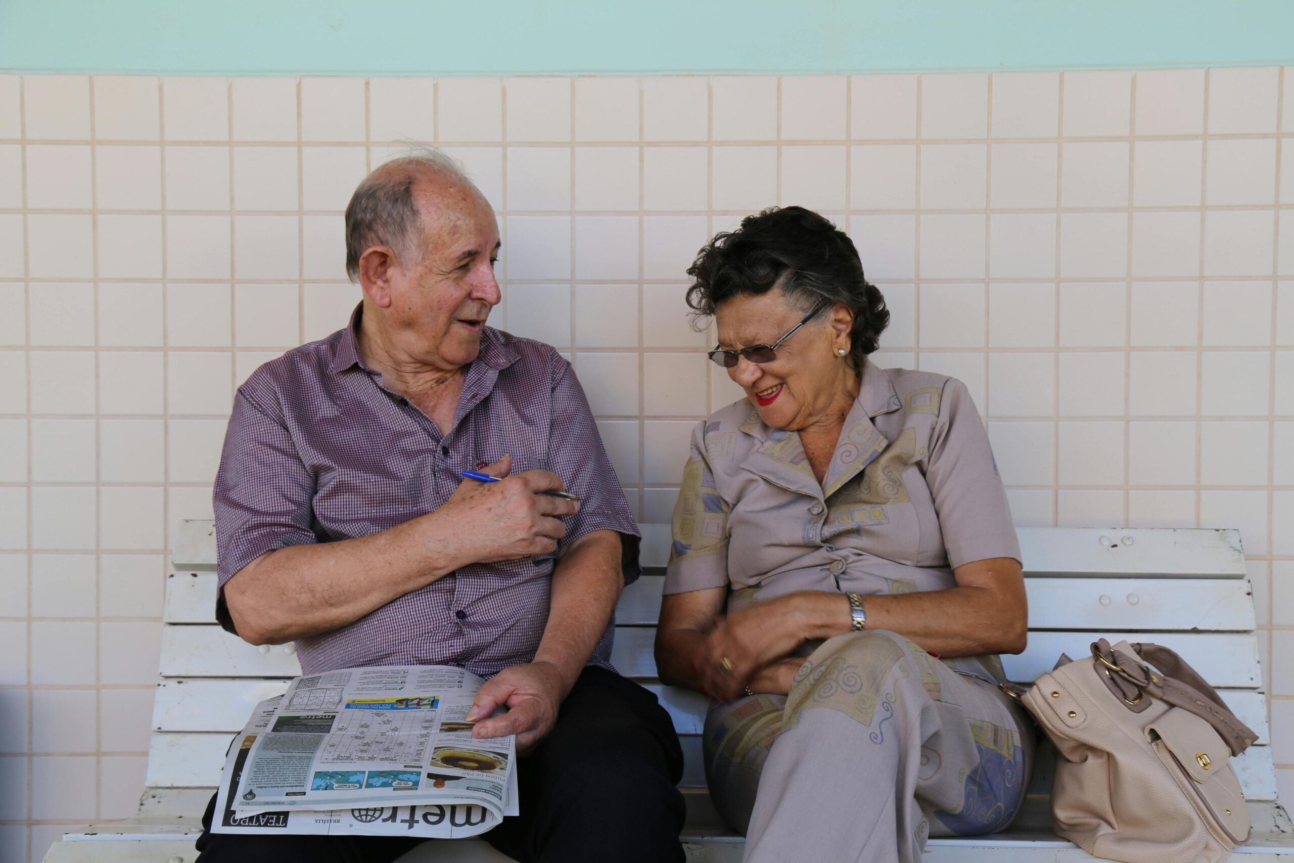 An elderly couple doing a crossword on a bench and laughing